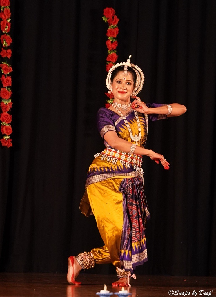 Odissi classical dancer Debashree Das performing in a purple and gold silk costume with traditional silver jewellery and headdress